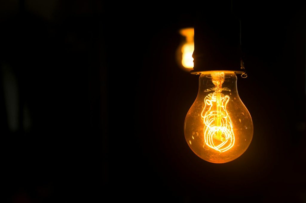 Close-up view of an illuminated vintage light bulb with glowing filament against a dark background.